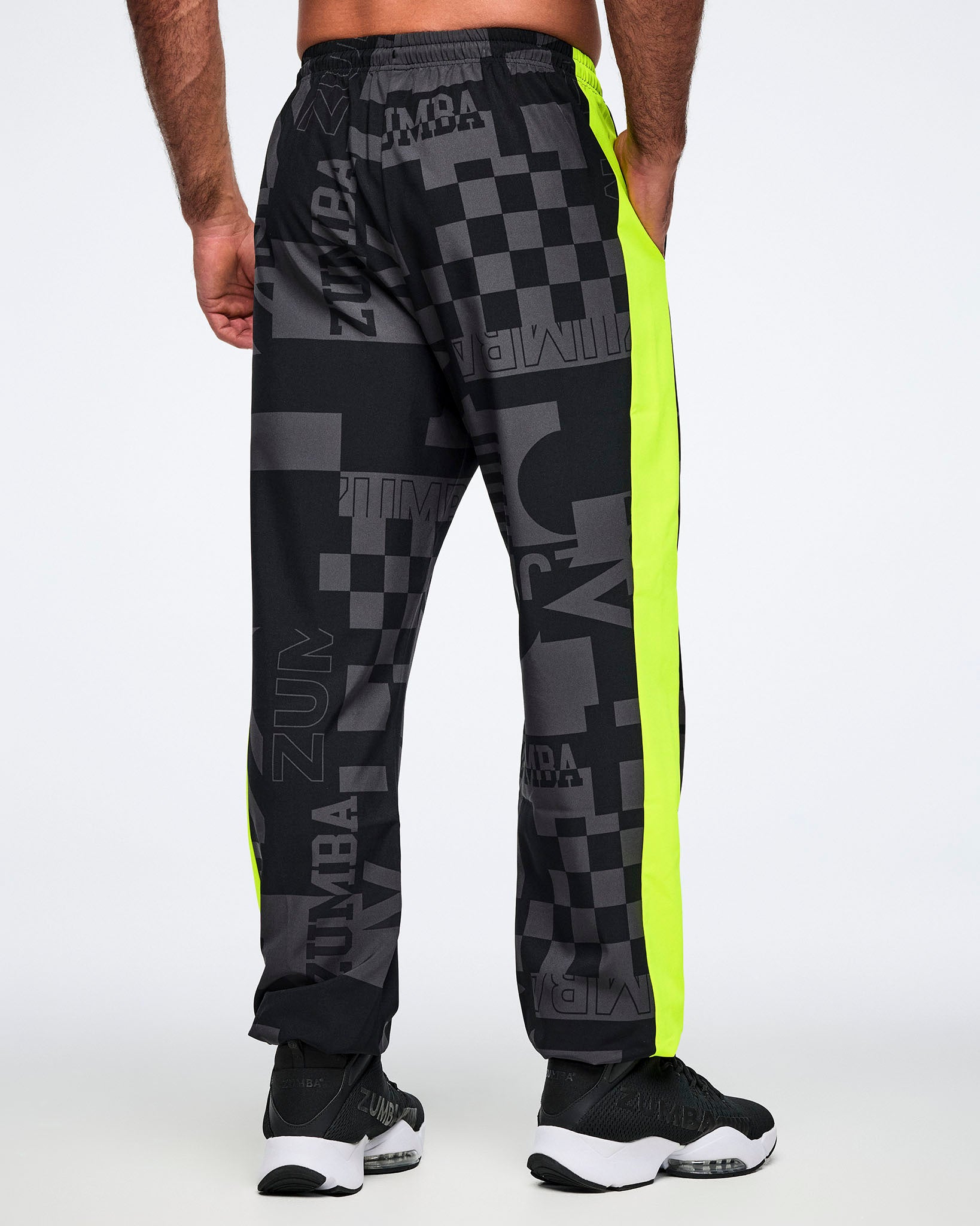 Back view of a male model wearing black and gray patterned pants with neon yellow stripes down the leg on a white background.