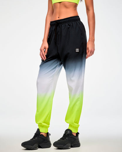 Female model wearing black-to-neon-yellow ombre joggers with a black cassette tag patch and black sneakers.