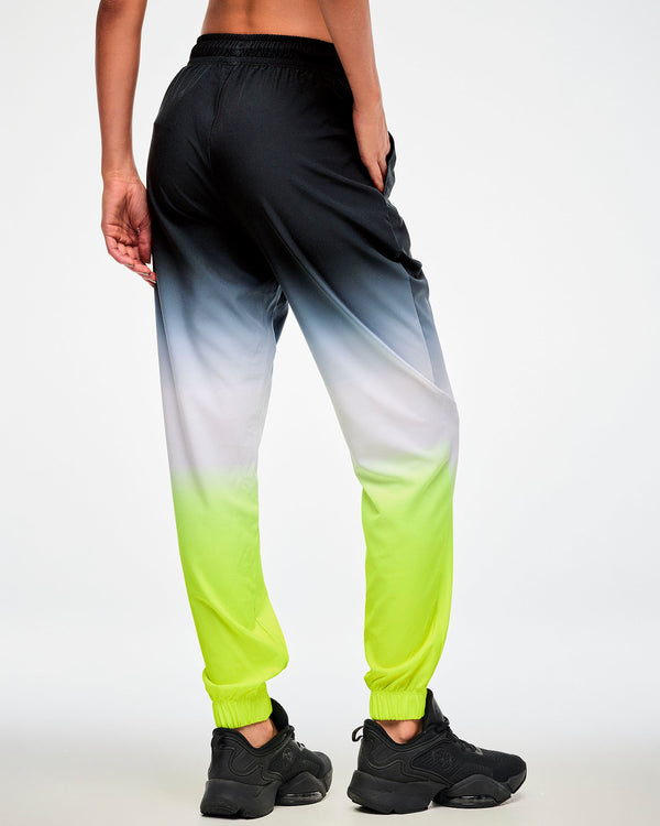 Shown from the back, female model wearing black-to-neon-yellow ombre joggers and black sneakers, hand in the side pocket.