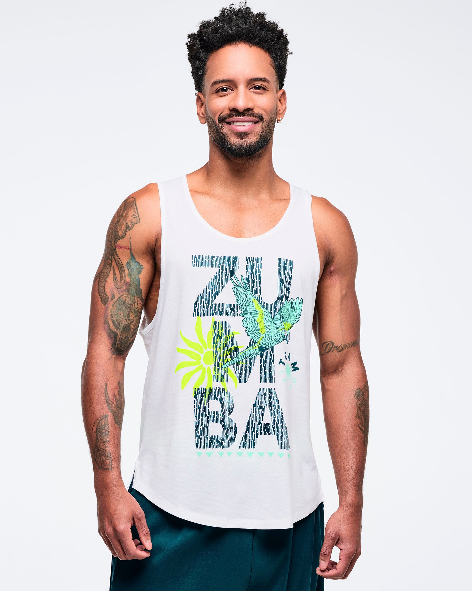 White racerback tank top with large “ZUMBA” text graphic, teal-and-lime parrot and sunburst print, worn by a male model with teal pants.