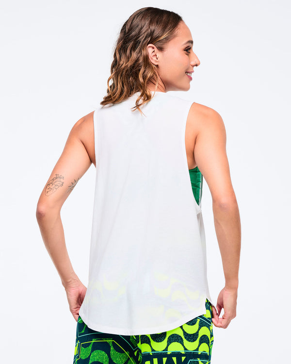 Back view of the white racerback tank on a female model, showing the solid back panel and curved hem, paired with green patterned leggings.