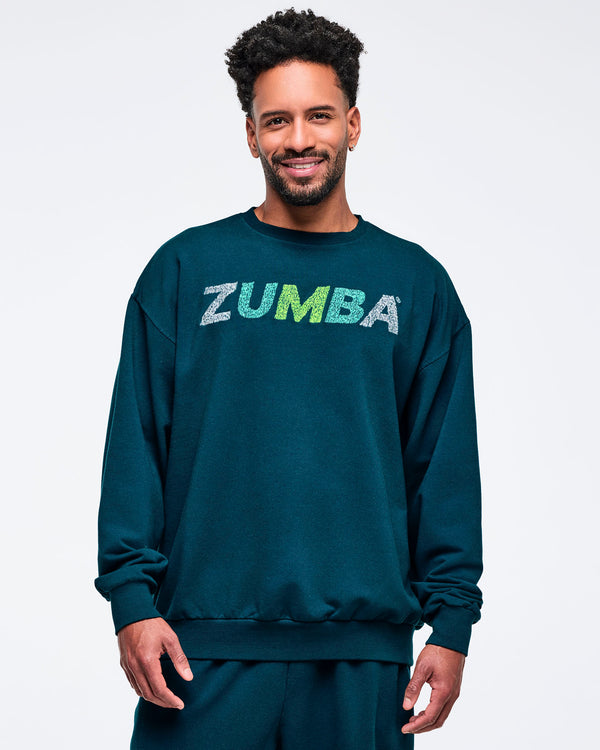 Teal oversized crewneck sweatshirt with ribbed cuffs and hem and a distressed “ZUMBA” logo on the chest, modeled by a male on a white studio background.