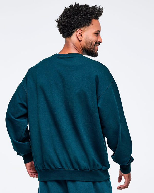 Back view of the teal crewneck sweatshirt showing a solid back and relaxed fit, modeled by a male on a white studio background.