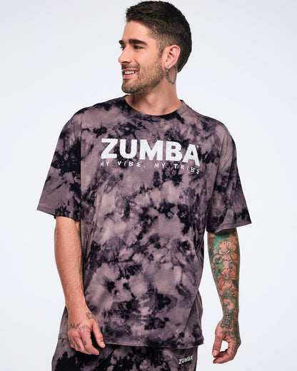 Oversized black and tan tie-dye Zumba T-shirt with a white “ZUMBA My Vibe. My Tribe.” graphic on the front, paired with matching tie-dye sweatpants. Male model wears the loose-fit short-sleeve crewneck tee with coordinating sweatpants.