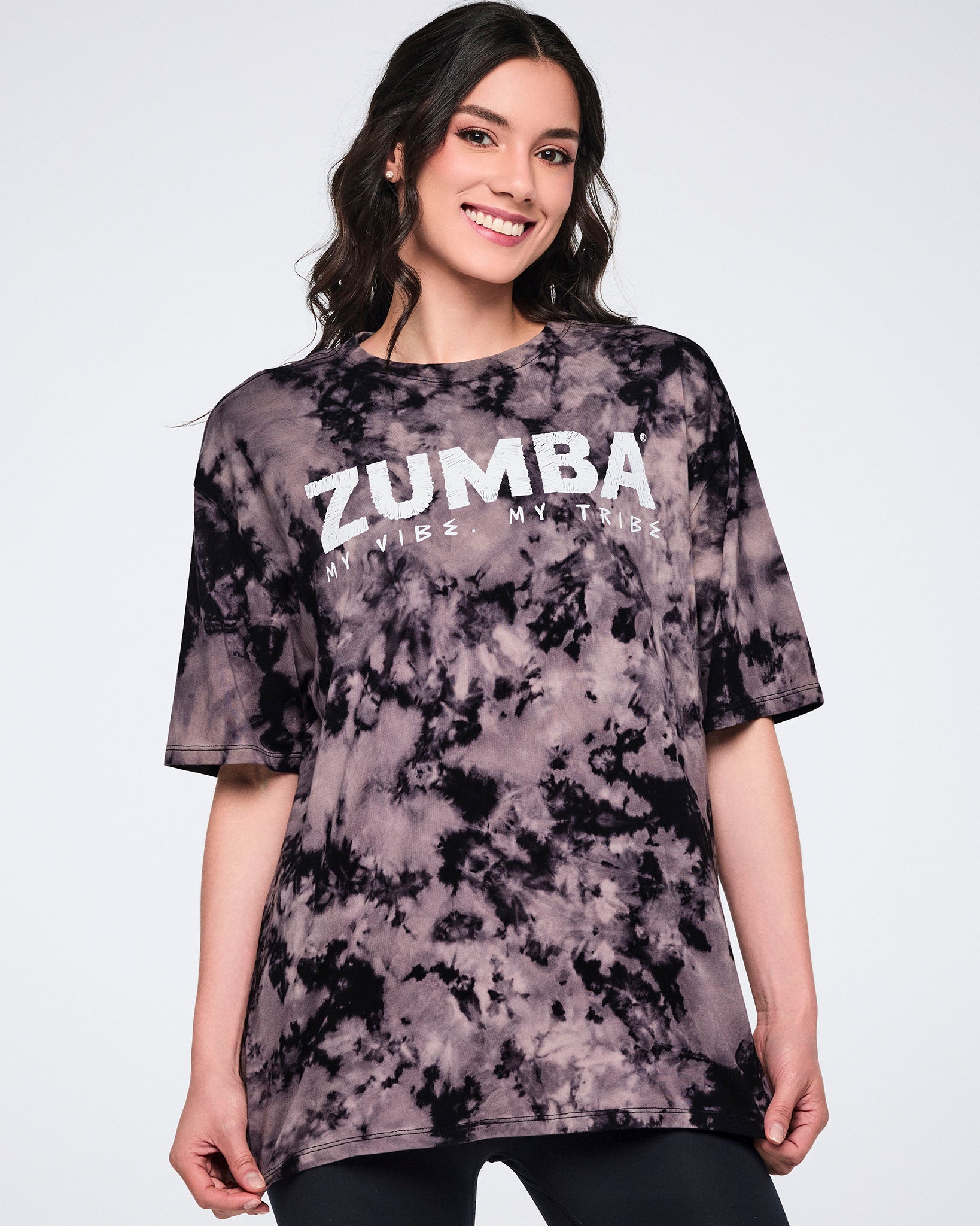Oversized black and tan tie-dye Zumba T-shirt with a white “ZUMBA My Vibe. My Tribe.” graphic on the front. Female model wears the loose-fit crewneck tee with short sleeves and black leggings.