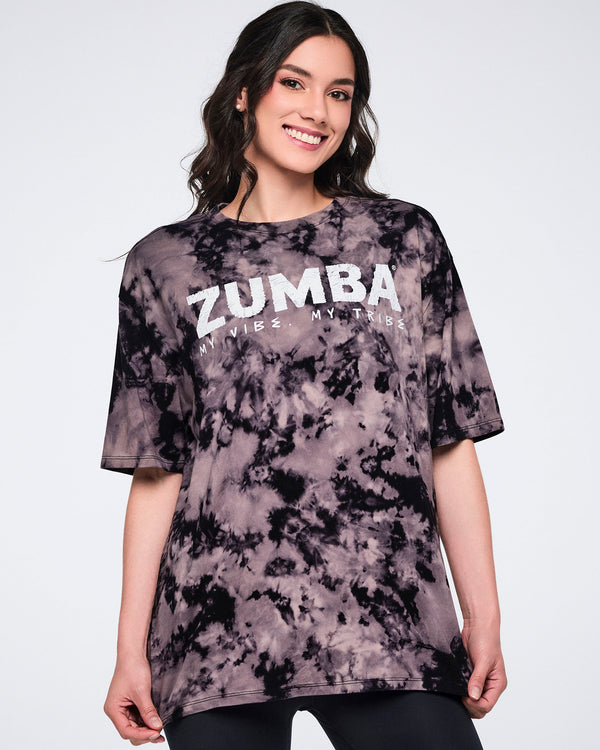 Oversized black and tan tie-dye Zumba T-shirt with a white “ZUMBA My Vibe. My Tribe.” graphic on the front. Female model wears the loose-fit crewneck tee with short sleeves and black leggings.