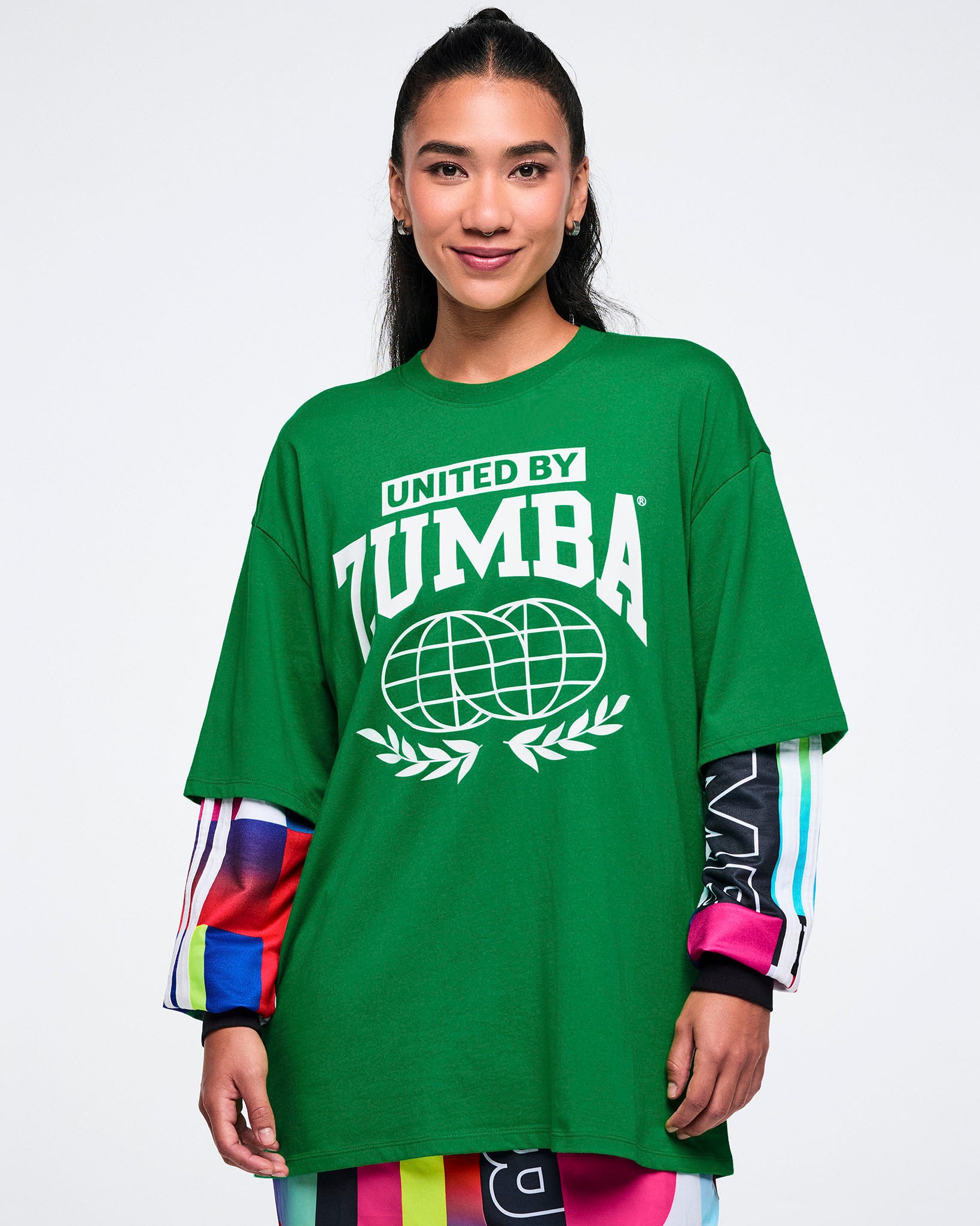 Female model wearing a green 'United by Zumba' t-shirt on a white background.