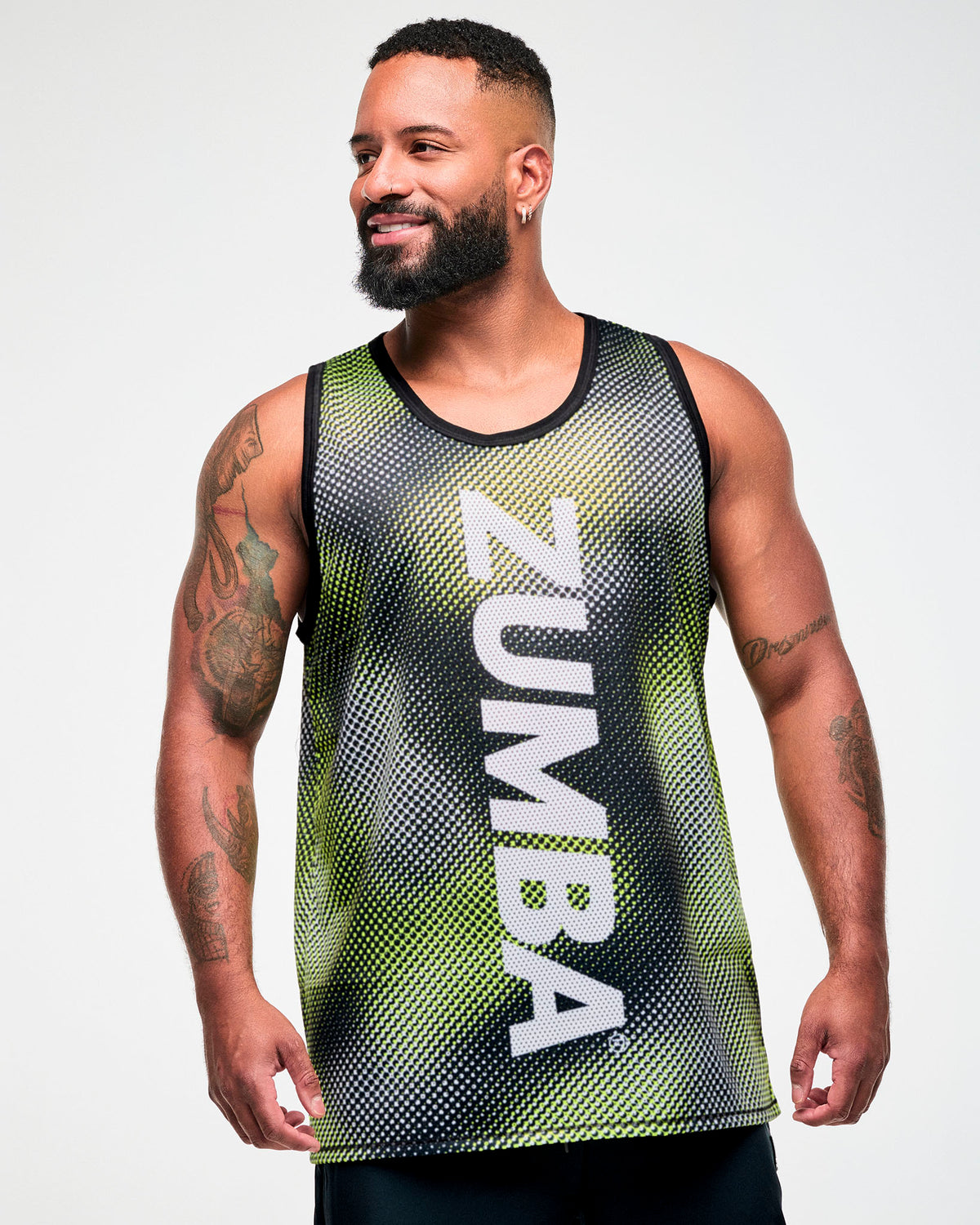 Male model wearing a black and yellow halftone dot-print tank top with "ZUMBA" in big vertical white text down the middle.