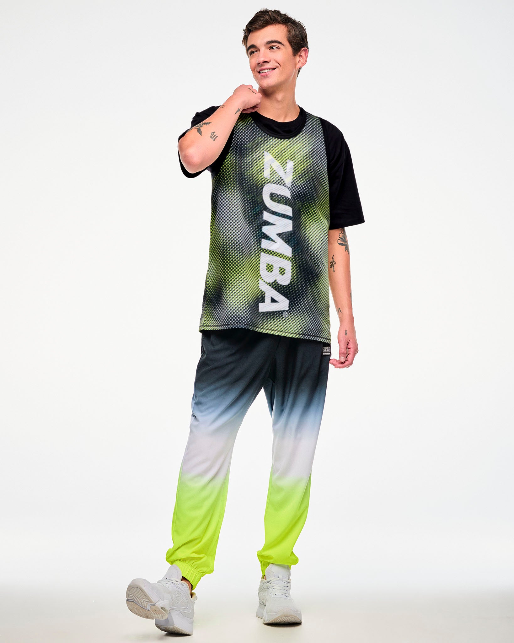 Full view of a male model wearing a black top with a yellow halftone dot-print panel, ombre joggers, and white sneakers.
