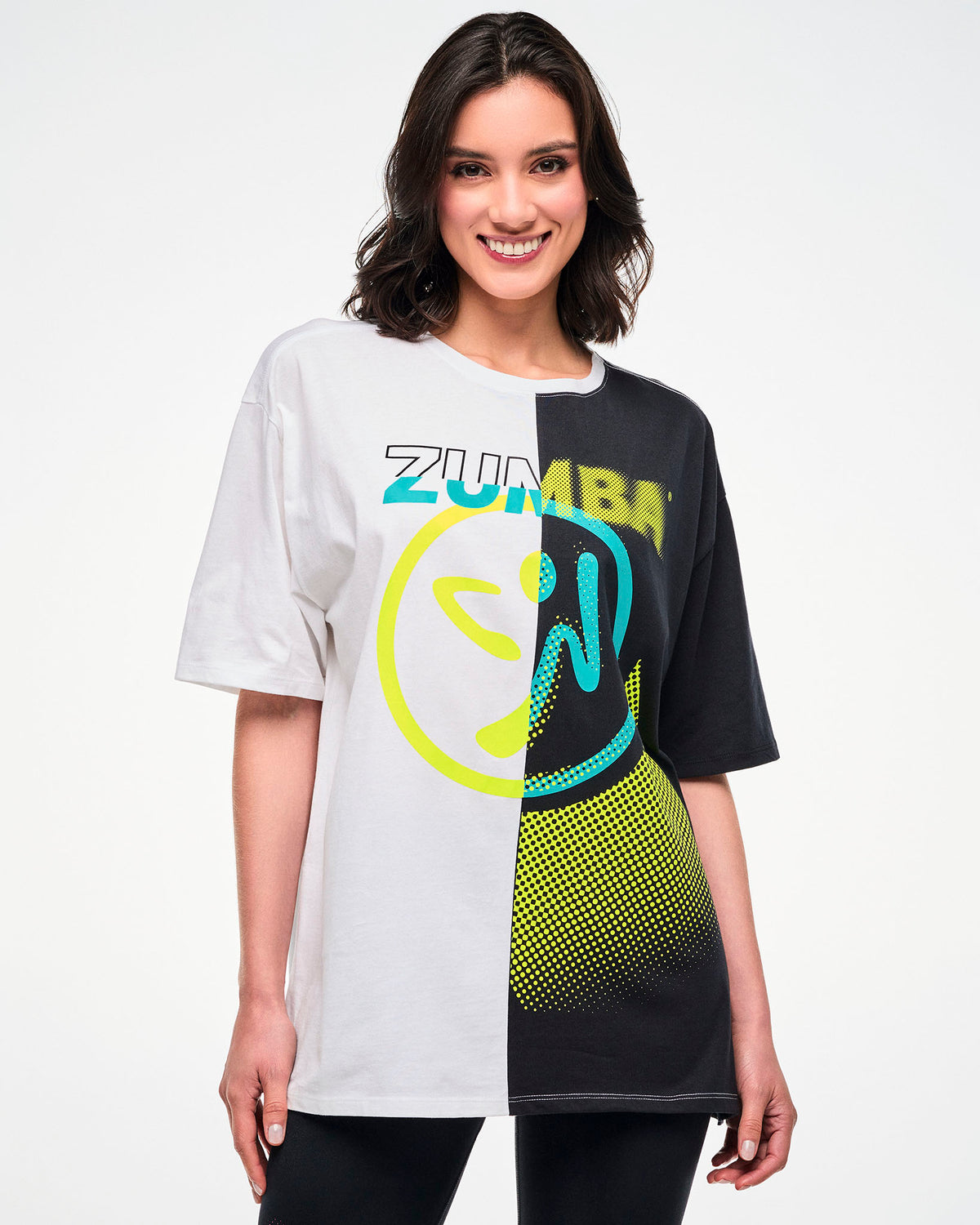 Female model wearing a black and white colorblock oversized T-shirt with a yellow and aqua "ZUMBA" Zumbito graphic.