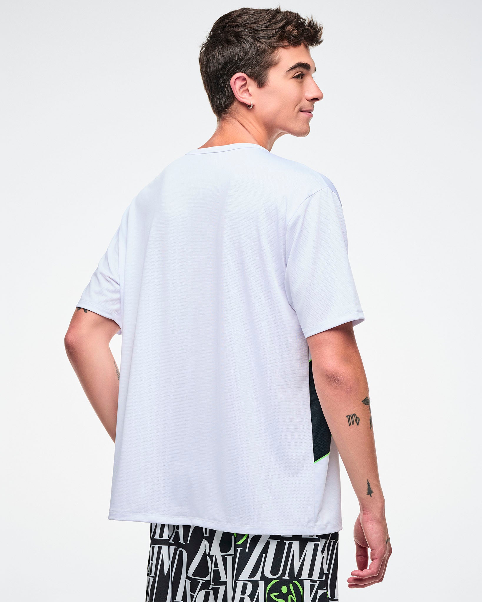 Back view of a male model wearing a white Zumba top on a plain background.