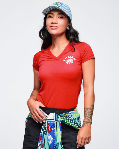 Light blue wavy-print baseball cap with curved brim and front “ZUMBA” palm-tree patch, modeled by a female wearing a red V-neck tee and a patterned jacket tied at the waist on a white studio background.