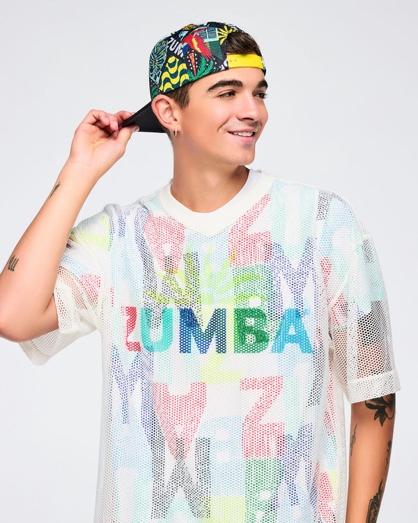 Male model wearing the cap backwards, showing the tropical-print panels and a bright yellow snapback closure; he’s in a white mesh tee with colorful “ZUMBA” lettering.