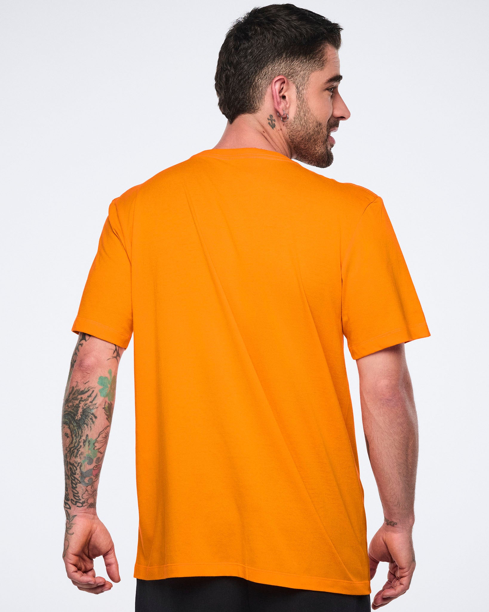 Male model shown from the back wearing an oversized bright orange short-sleeve T-shirt with a relaxed fit, paired with black bottoms.