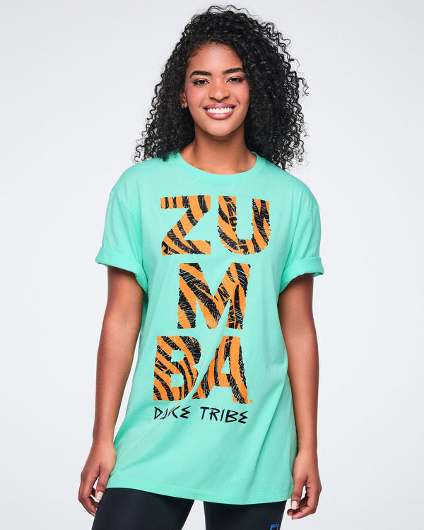 Female model wearing an oversized mint green Zumba T-shirt with rolled short sleeves, a bold orange-and-black zebra-print “ZUMBA” graphic, and “Dance Tribe” text, paired with black leggings.