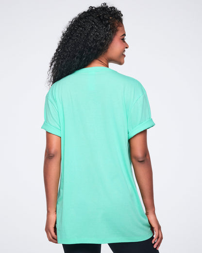 Female model shown from the back wearing an oversized mint green T-shirt with rolled short sleeves and a long relaxed fit, paired with black leggings.
