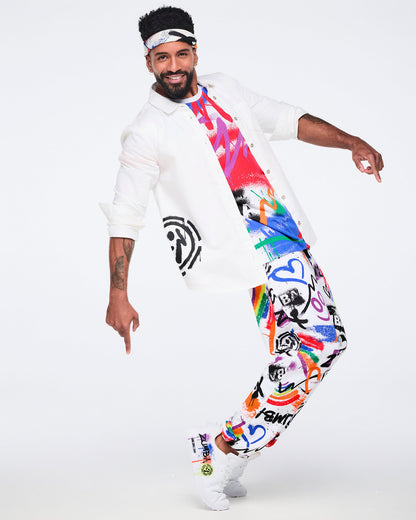 Male model wearing a bandana on this head, a white button‑down shirt, colorful graphic tee, matching graphic pants, and white Zumba shoes against a white background.