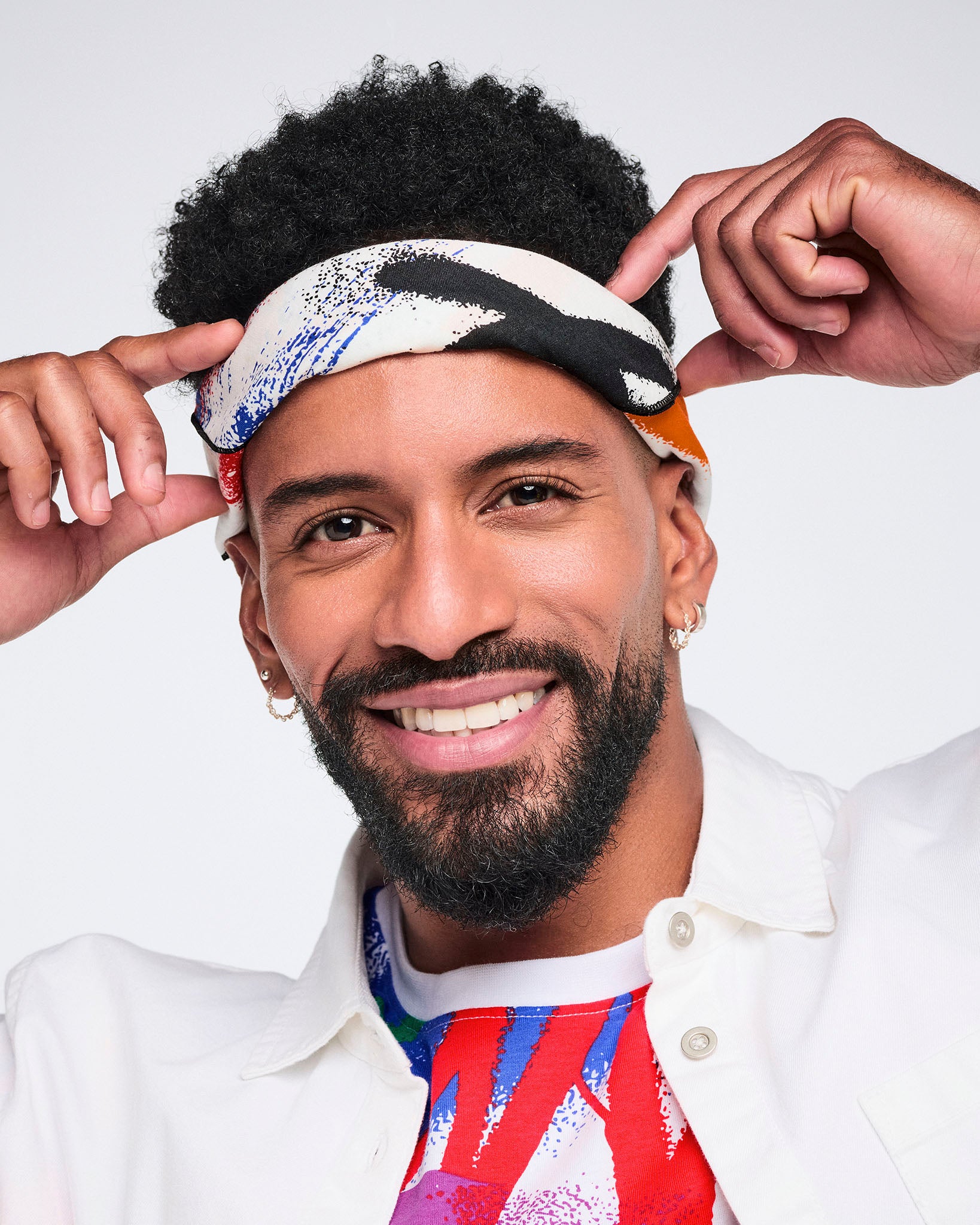 Close up of a male model adjusting a colorful bandana against a white background.