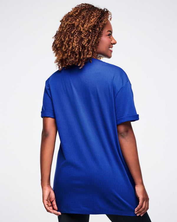 Back view of a female model wearing a blue t-shirt on a white background.