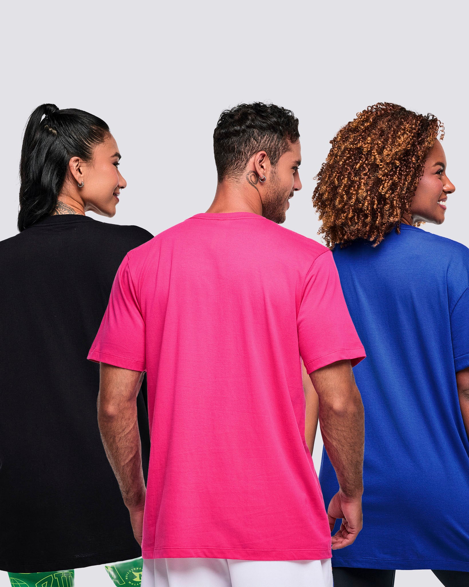 Back view of three models—two female, one male—wearing vibrant Zumba T-shirts on a white background.