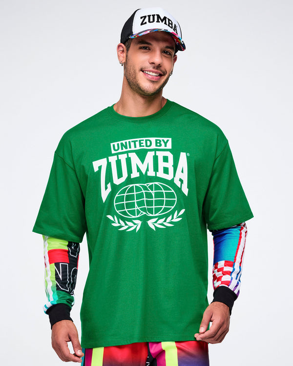 Male model wearing a green 'United by Zumba' t-shirt with with a white hat with a colorful bill, on a white background.