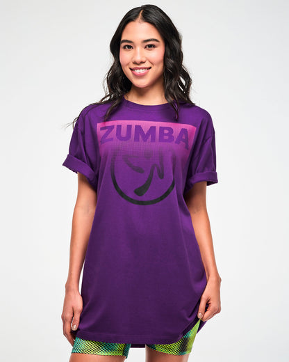 Female model wearing a purple T-shirt with a pink "ZUMBA" logo and black Zumbito graphic.