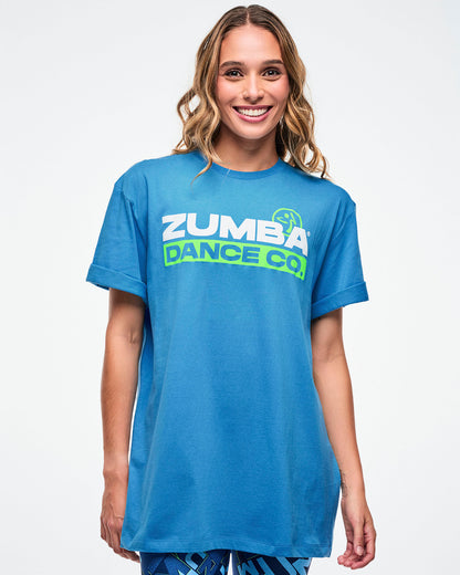 Female model wearing a light blue Zumba t-shirt on a white background.