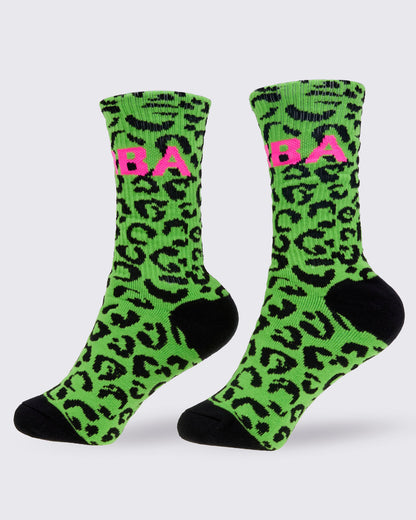 A pair of high socks, from the left side featuring a bright green and black leopard print pattern, with a pink 'ZUMBA' text on the top and solid black toes and heels, shown against a white background.