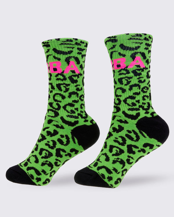 A pair of high socks, from the left side featuring a bright green and black leopard print pattern, with a pink 'ZUMBA' text on the top and solid black toes and heels, shown against a white background.