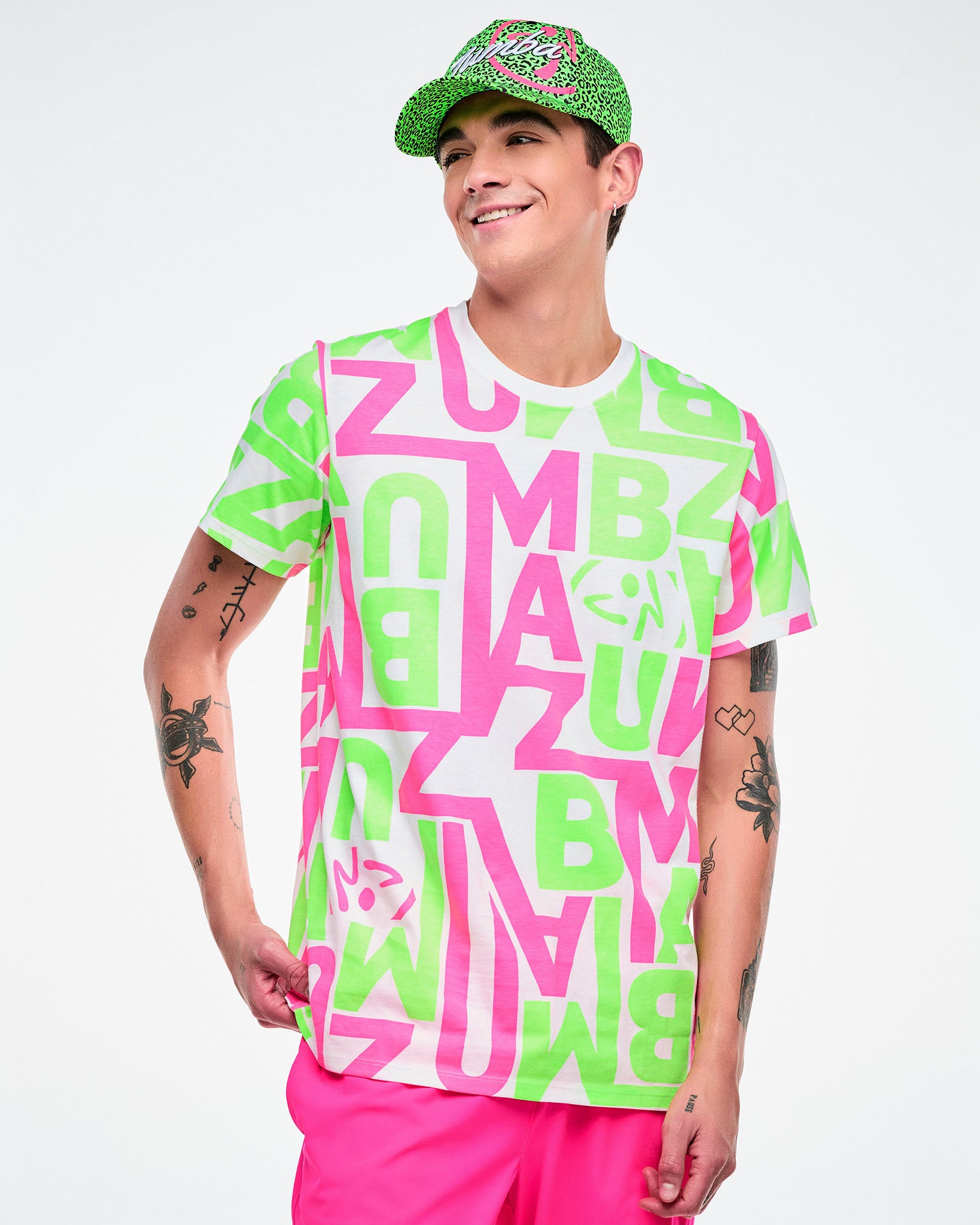 Male model wearing a Zumba green and black leopard print hat, bright green and pink and white graphic tee and pink pants.