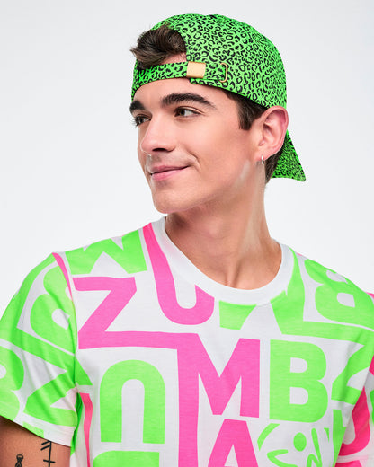 Male model wearing a green-and-black leopard-print hat turned backward, showing the metal closure, paired with a multicolored Zumba shirt.