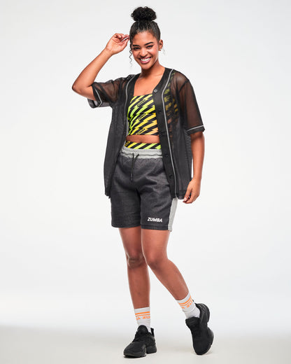 Female model wearing black and grey shorts, black shoes and paired with a sheer black button-up top and printed crop top.