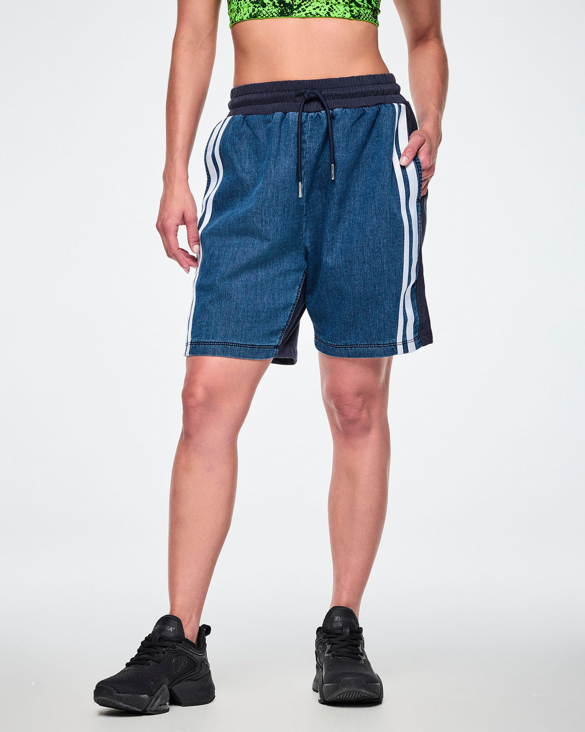 Front view of a female model wearing denim combo shorts with an elastic waistband, drawcord, and double white stripe along the leg.