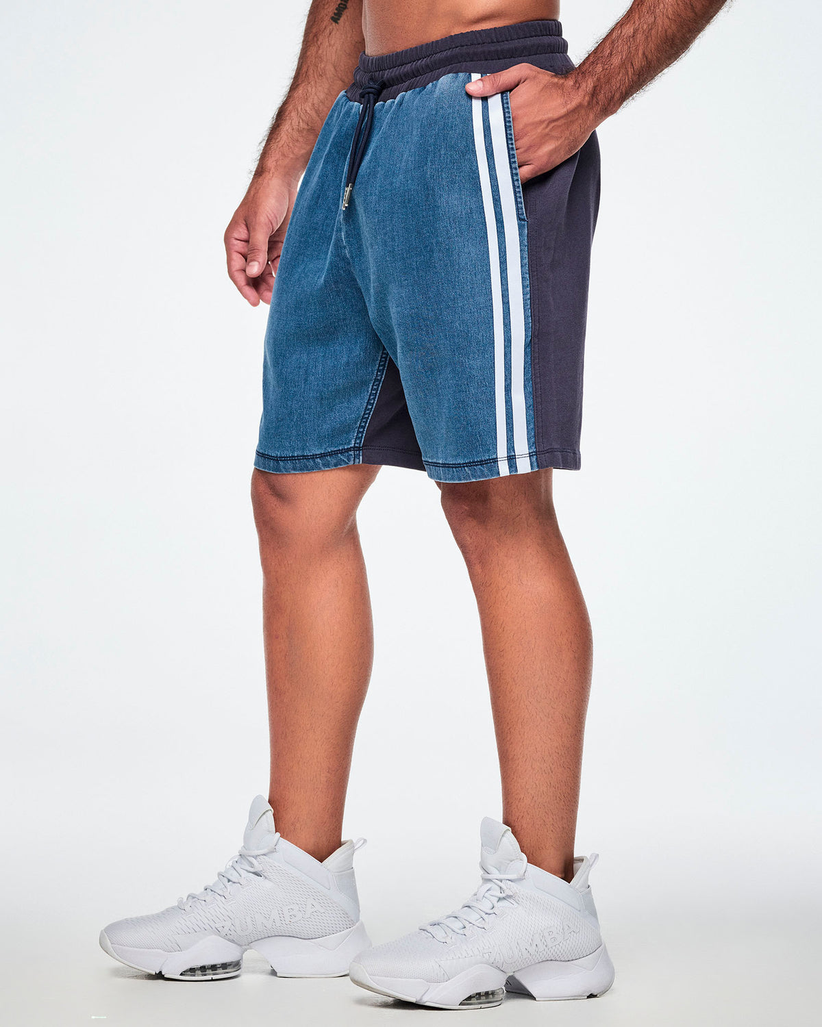 Side view of a male model wearing denim combo shorts, showing the denim front leg panel with a double white stripe against the navy back.