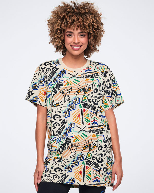 Cream short-sleeve graphic T-shirt with a crew neckline, oversized fit, and allover multicolor abstract print featuring geometric shapes, animal-inspired motifs, and Zumba logos. Female model wears the T-shirt over black leggings.