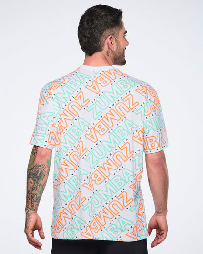 Back view of a white short-sleeve Zumba T-shirt with a crew neckline and allover mint and orange diagonal logo print. Male model wears the relaxed-fit tee with black pants.