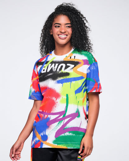 Female model wearing a colorful graphic t-shirt with visible brand logo on a plain background.