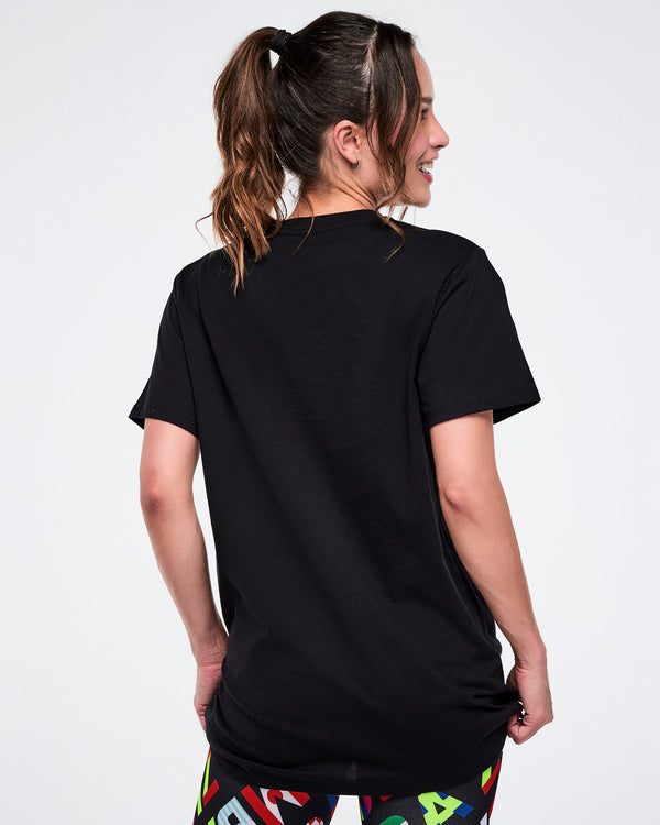 Back view of female model wearing a black t-shirt with colorful leggings on a white background.