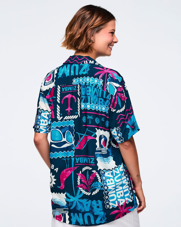 Back view of a navy short-sleeve button-up shirt with a teal, white, and hot pink allover Zumba beach-and-nautical graphic print; shown on a female model with white shorts.
