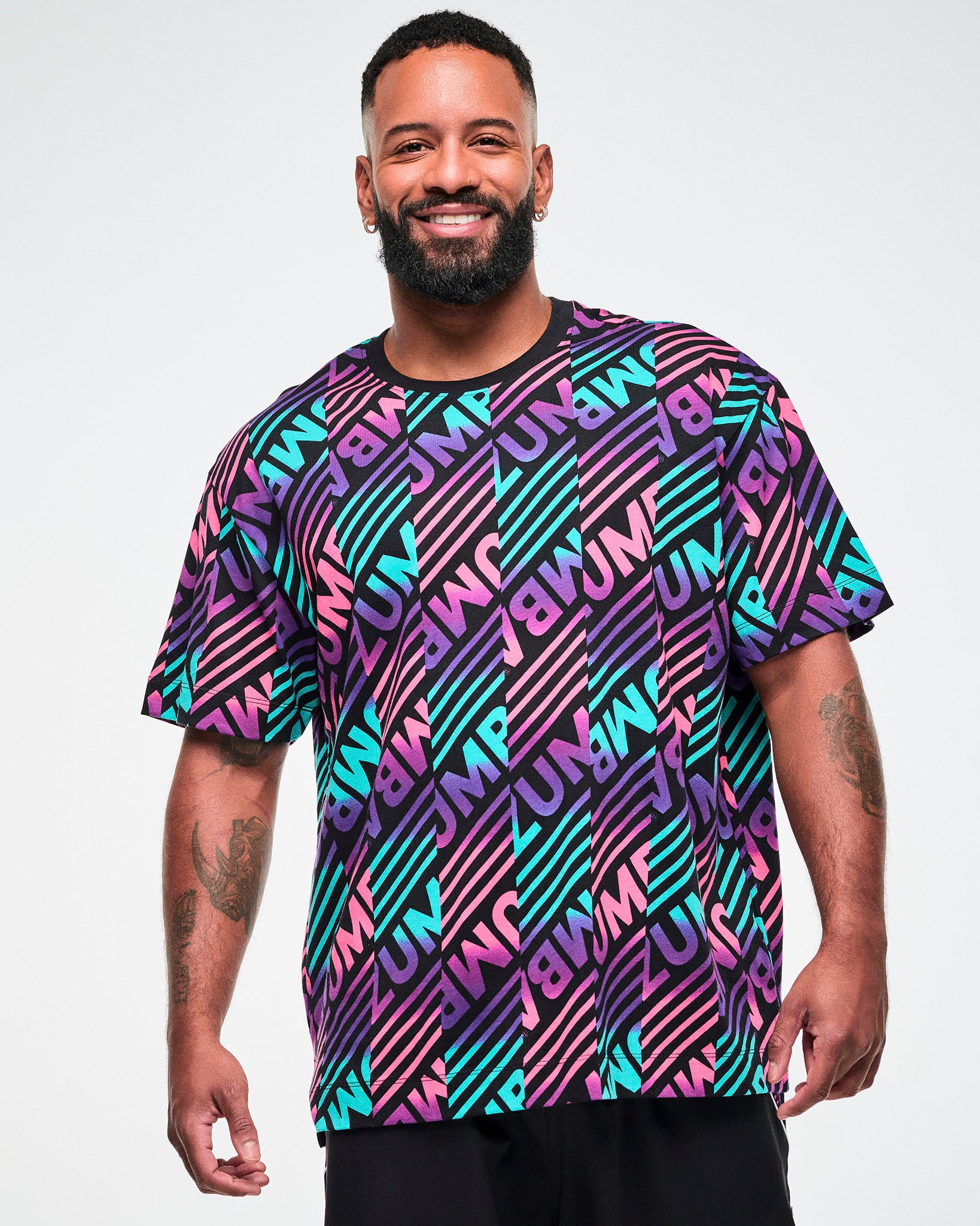 Male model wearing a black tee with a colorful pink, aqua, and purple diagonal striped "ZUMBA" broken-pattern print.