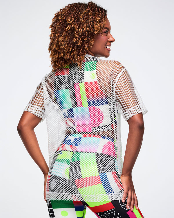 Back view of a female model in a colorful bra and biker shorts, layered with a white mesh top, set against a white background.