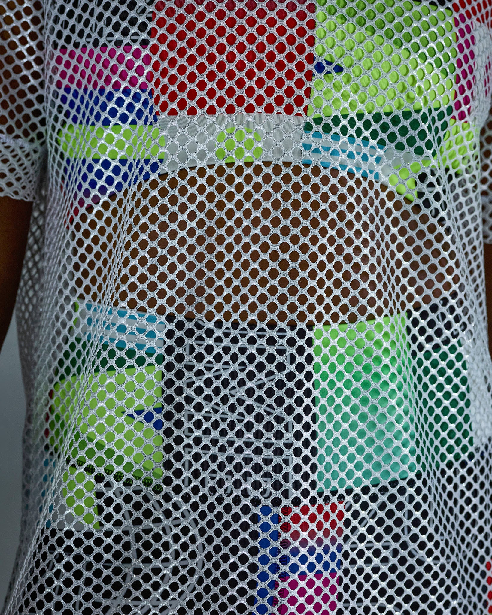 Close-up of the silver mesh fabric with multicolored patterns of an outfit underneath.