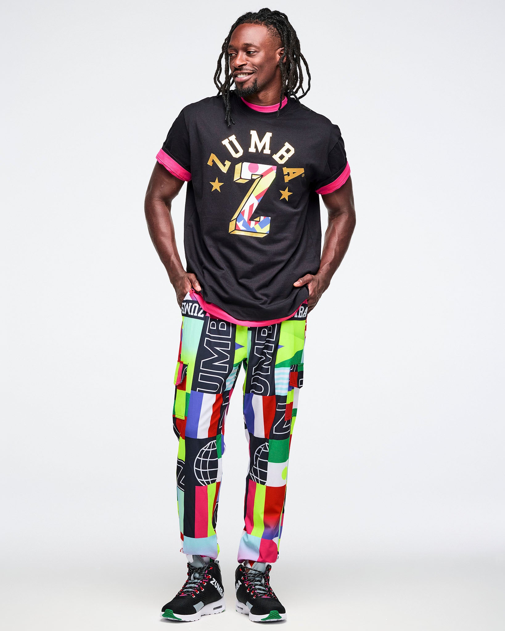 Male model wearing a black t-shirt with colorful graphics and multicolored pants on a white background.
