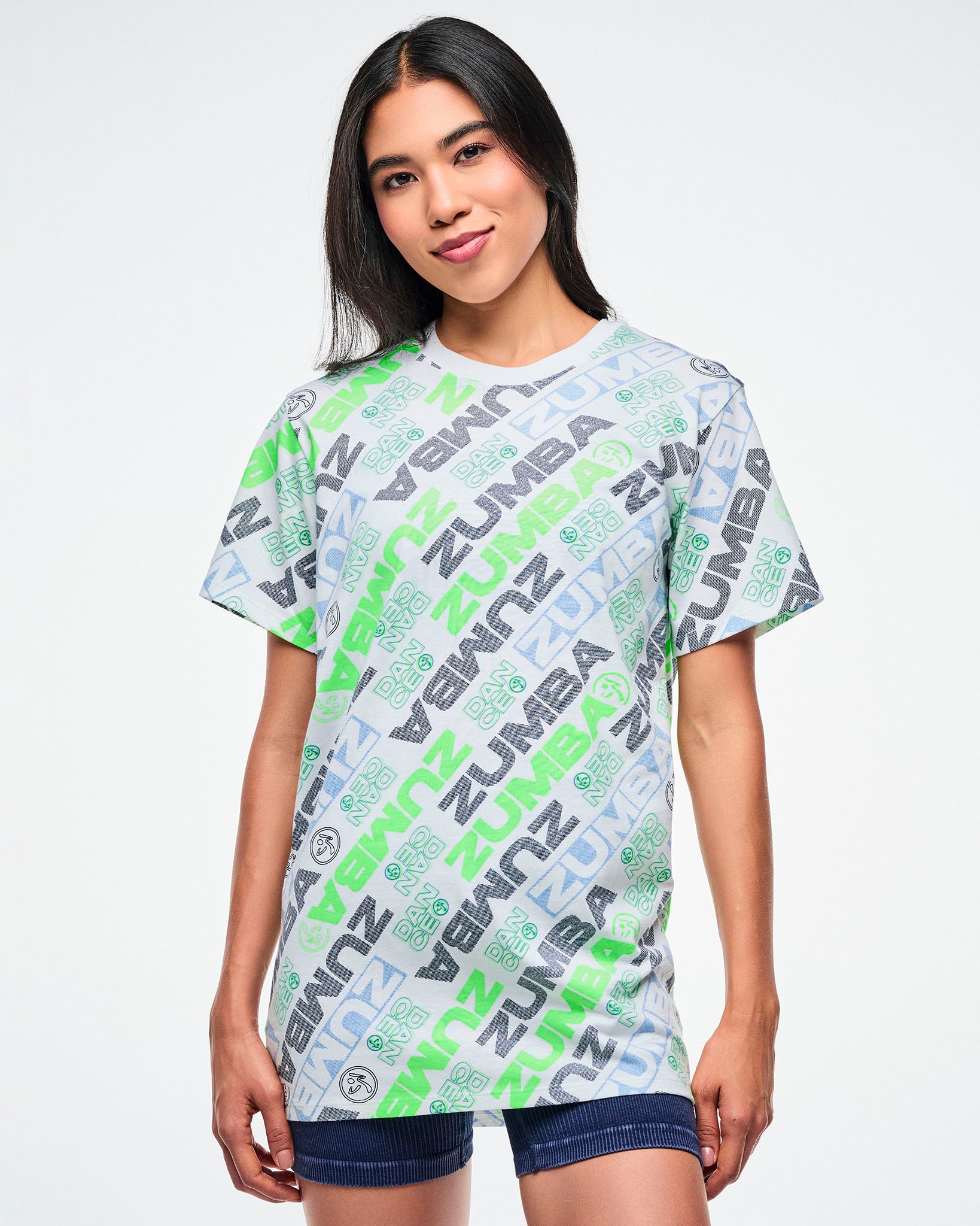 Female model wearing a Zumba tee with a blue and green 'ZUMBA' logo pattern on a white background.