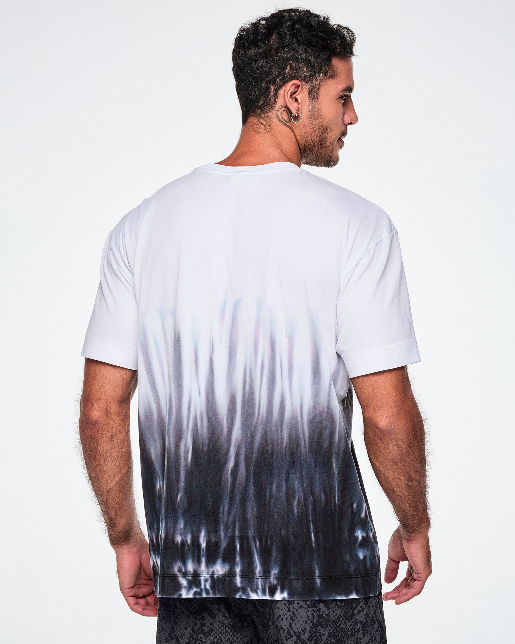 Back view of a male model wearing a white tee with a black-to-white tie-dye flame pattern at the bottom, posed against a white background.