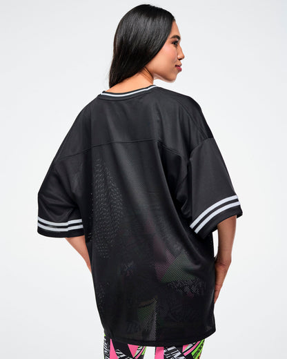 Back view of a female model wearing a black Zumba jersey paired with matching patterned leggings on a white background.