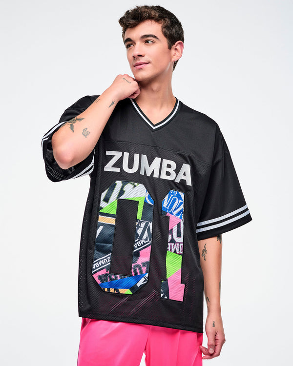 Male model wearing a black Zumba jersey with silver “ZUMBA” text and a large colorful patterned “01,” paired with pink pants.