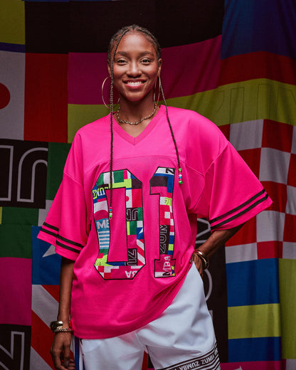 Female model wearing a bright pink mesh jersey with colorful patterns against a multicolored background.