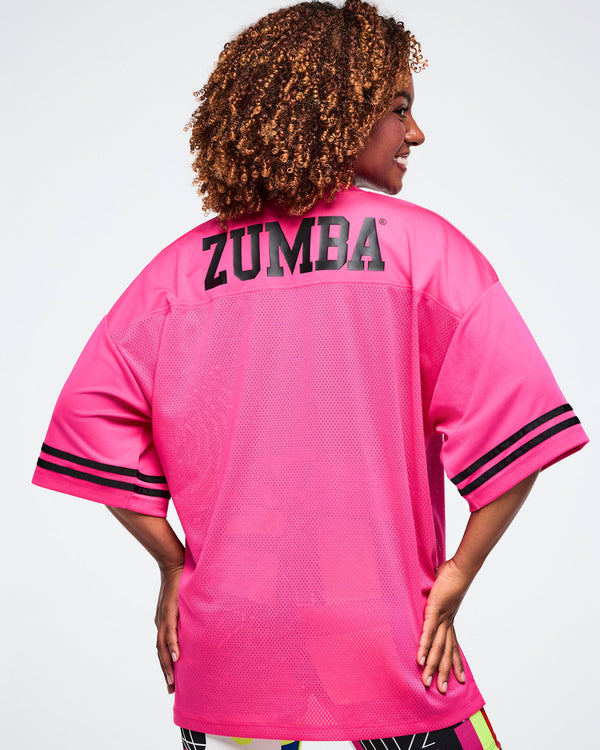 Female model, shown from the back, wearing a pink Zumba mesh top with 'Zumba' printed on the back in black.