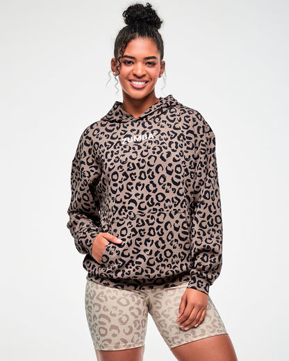 Female model smiling in the leopard print hooded pullover sweatshirt, showing its oversized fit and dropped shoulders, paired with beige leopard print biker shorts.
